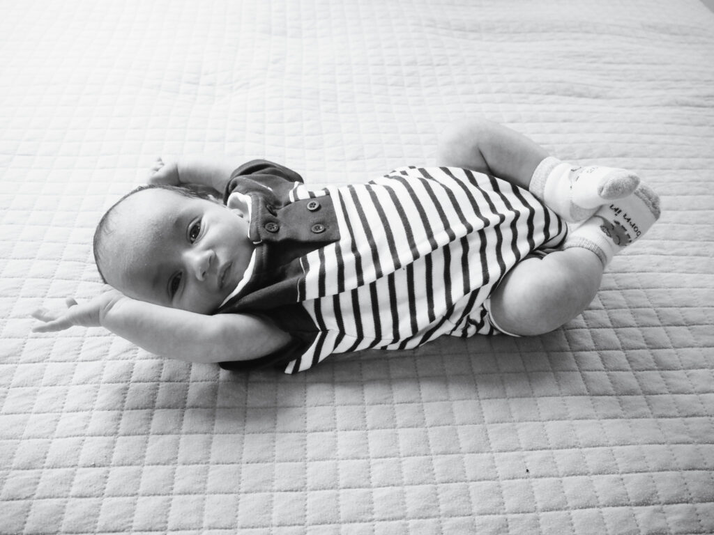 B&W image of newborn laying on bed looking at camera