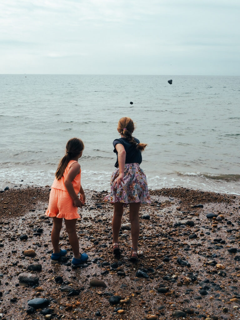Sisters throwing pebbles into sea