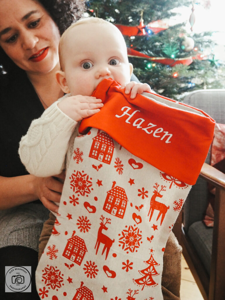 mum holding baby who is holding Christmas stocking
