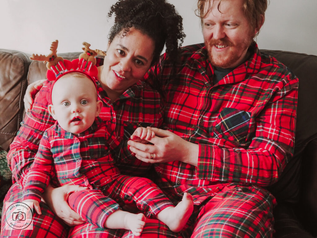 Mum and baby looking at camera sitting with Dad wearing Christmas pyjamas